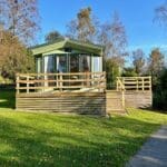 Green holiday caravan with a wooden deck on a grassy hillside