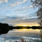 Sunset over a calm lake with reflections of trees and clouds in the water
