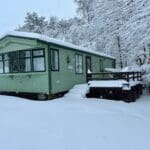 A cozy green cabin covered in a thick layer of snow