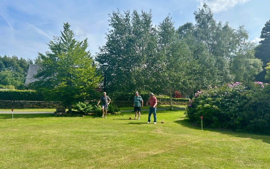 Three people playing croquet in a garden