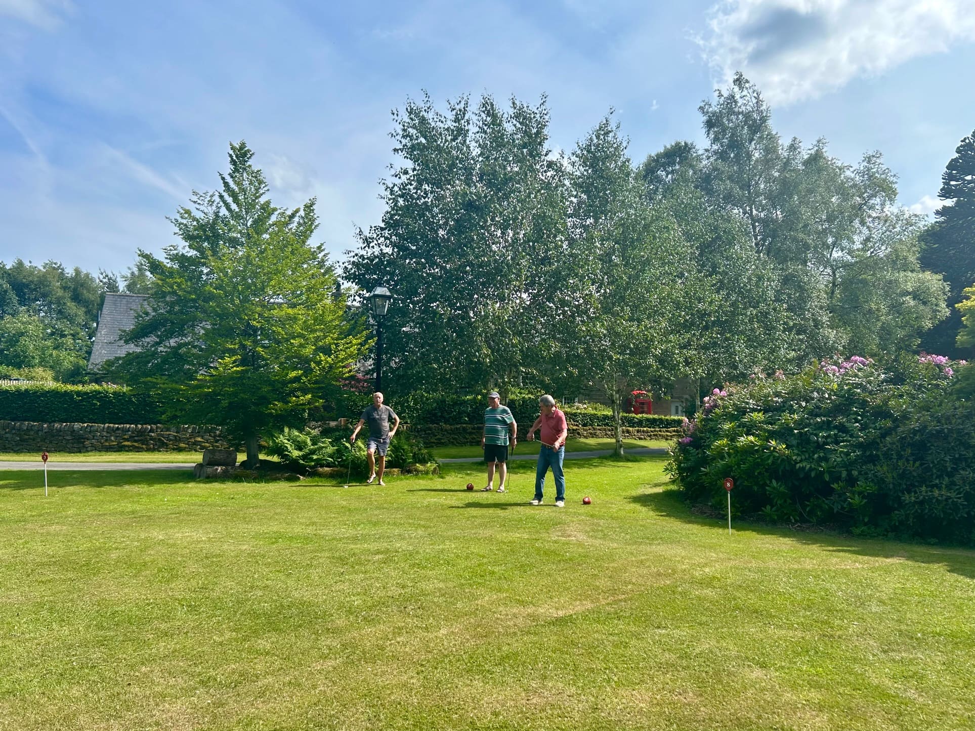 Three people playing croquet in a garden