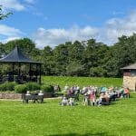 Outdoor performance in a bandstand with people seated at Warren Forest Park