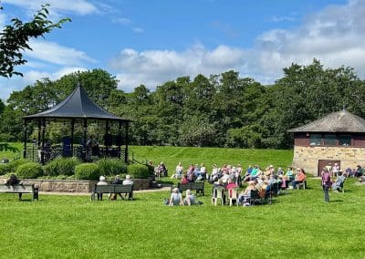 Outdoor performance in a bandstand with people seated at Warren Forest Park